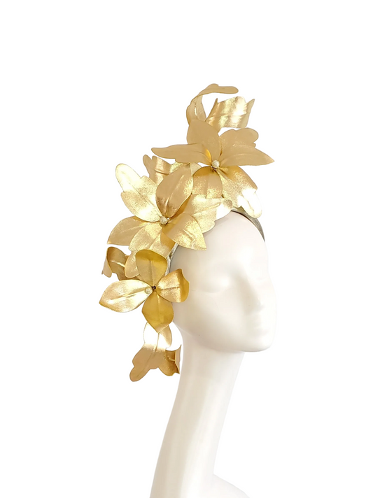 A gold metallic floral fascinator headpiece displayed on a white mannequin head against a plain light gray background.