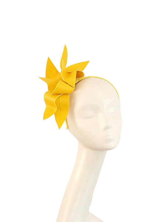 A bright yellow fascinator headpiece displayed on a white mannequin head against a plain off-white background.