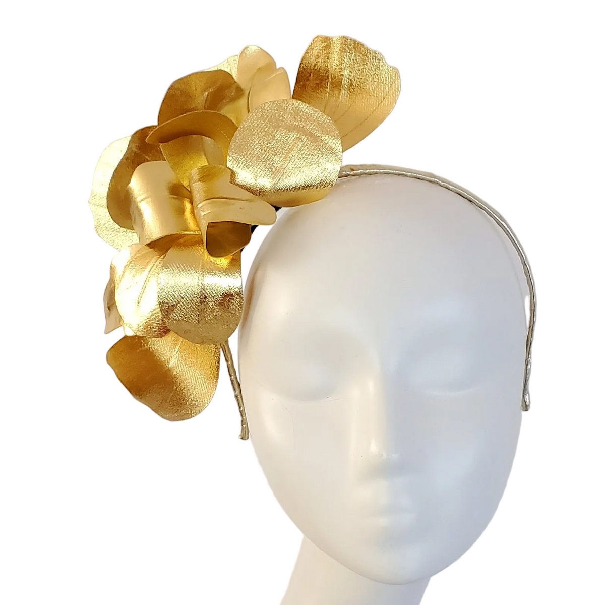 A gold metallic flower fascinator headpiece displayed on a white mannequin head against a light gray background.