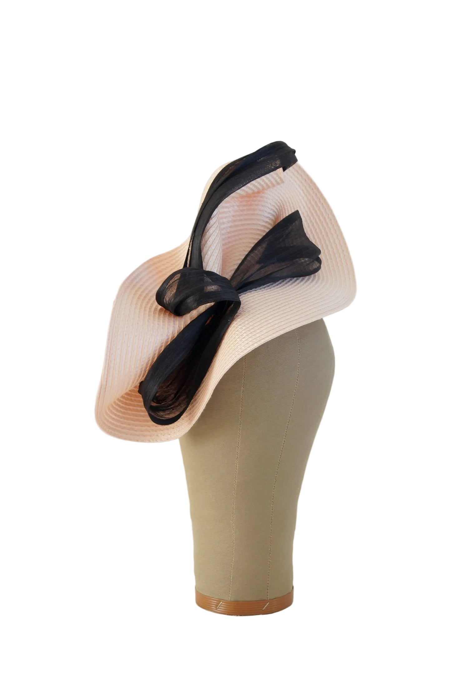 A pale blush pink pleated fascinator hat with a large black mesh bow, displayed on a beige mannequin head against a plain off-white background.
