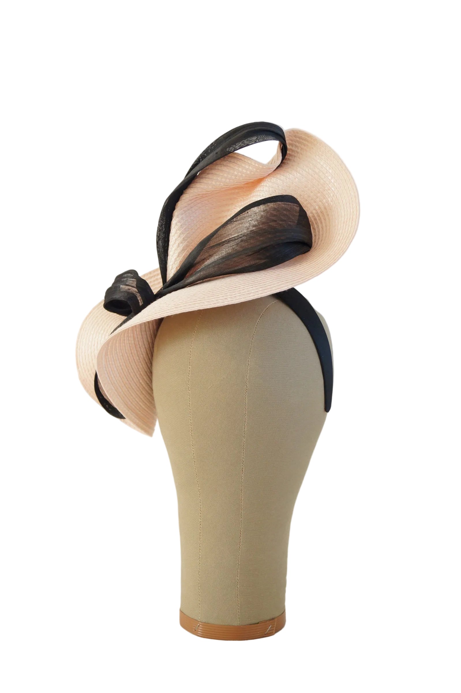 A pale blush pink fascinator hat with black mesh and ribbon accents, displayed on a beige mannequin head against a light gray studio background.