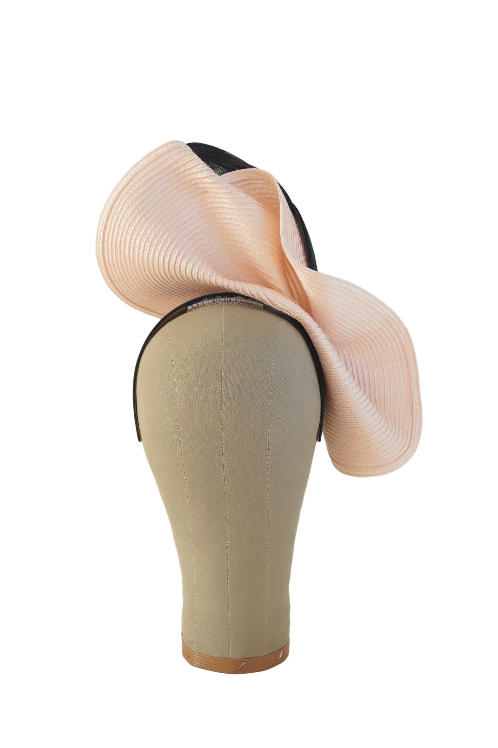 A large structured fascinator in pale blush pink with a black band, displayed on a beige fabric mannequin head against a plain white studio background.