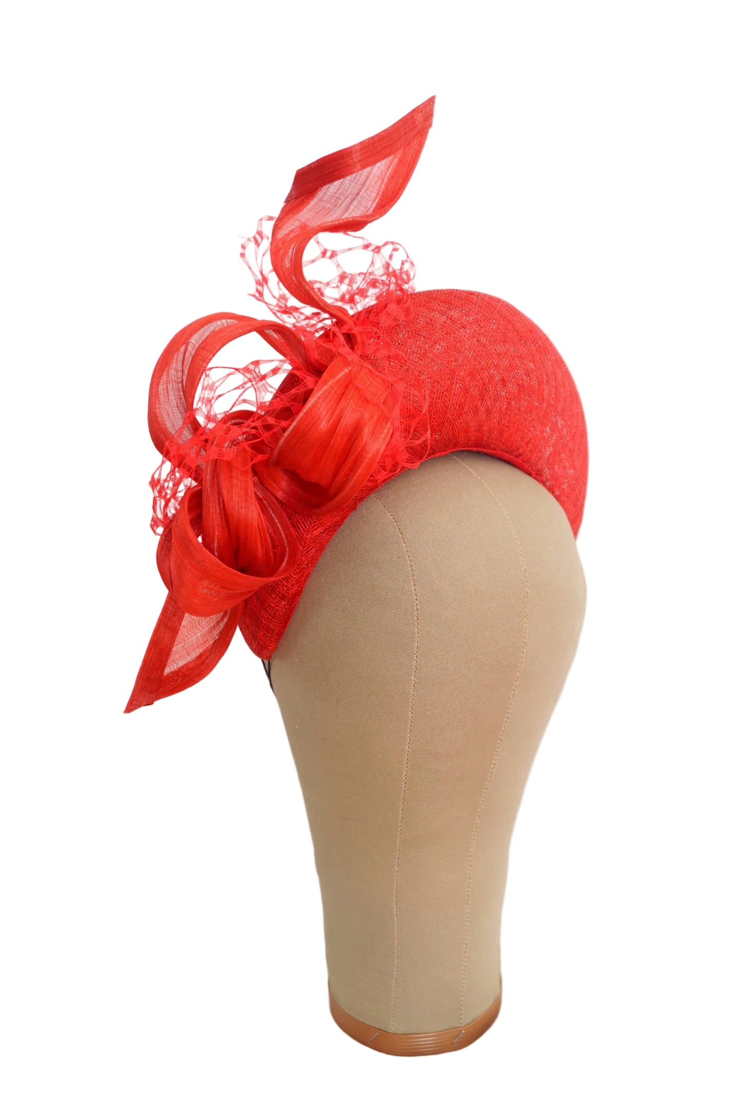 A bright red fascinator hat with large ribbon loops, sheer mesh, and lace detailing, displayed on a beige mannequin head against a white background.