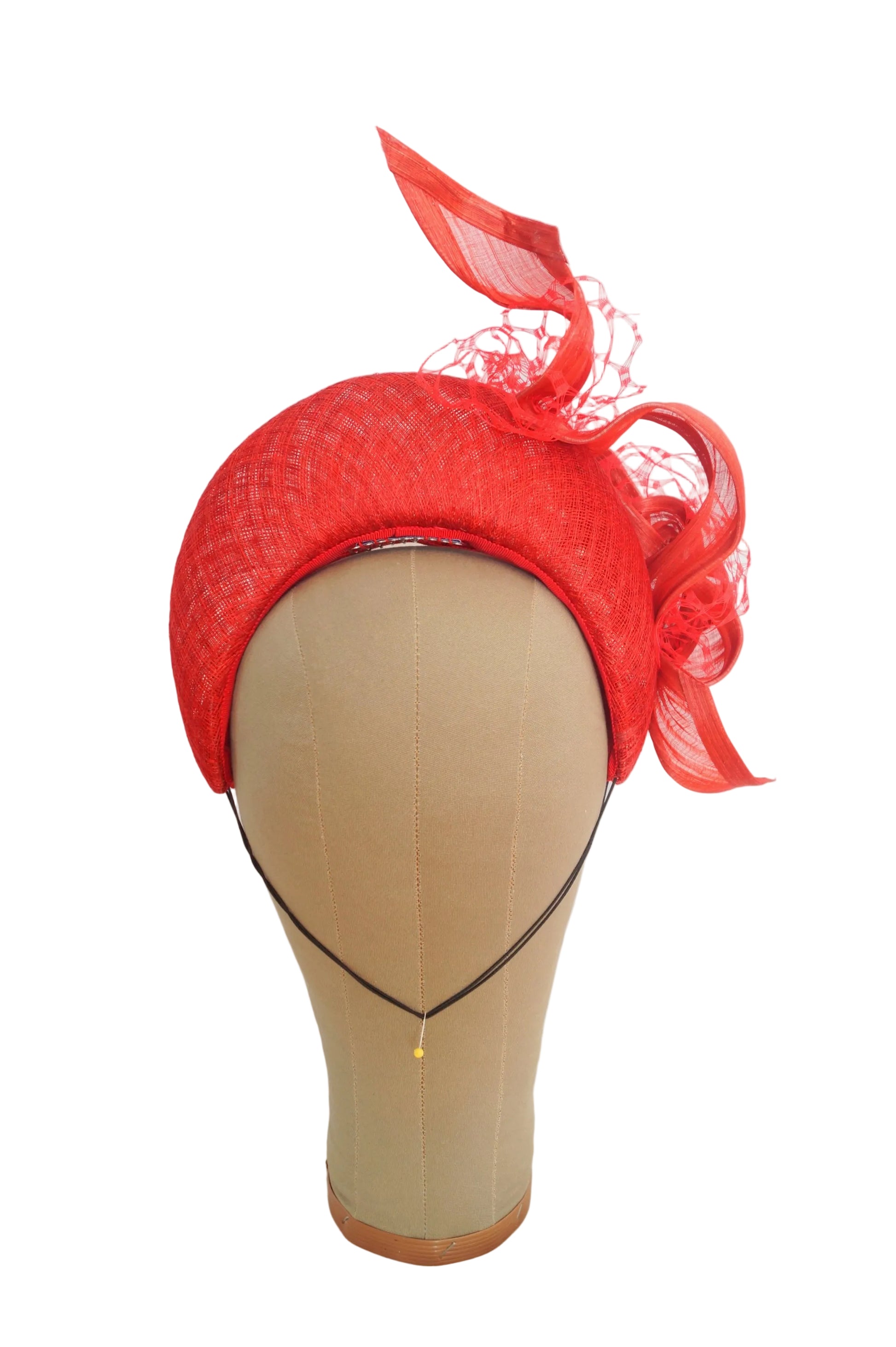 A bright red fascinator hat with ribbon loops, and a matching fascinator net, displayed on a beige mannequin head against a white backdrop.